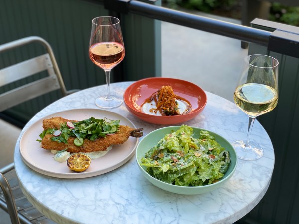 A small table is set with two wine glasses filled with white and rosé. Three dishes, including a salad and a fish meal sit on decorated plates.
