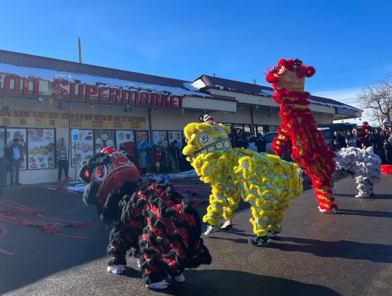 Four Chinese lion dancers in black, yellow, red and white costumes jump in the air.