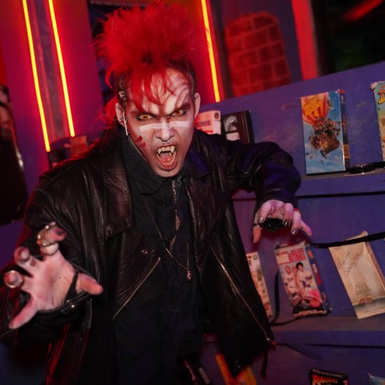 A person wearing vampire make up with a red mohawk makes a scary face in the haunted house.