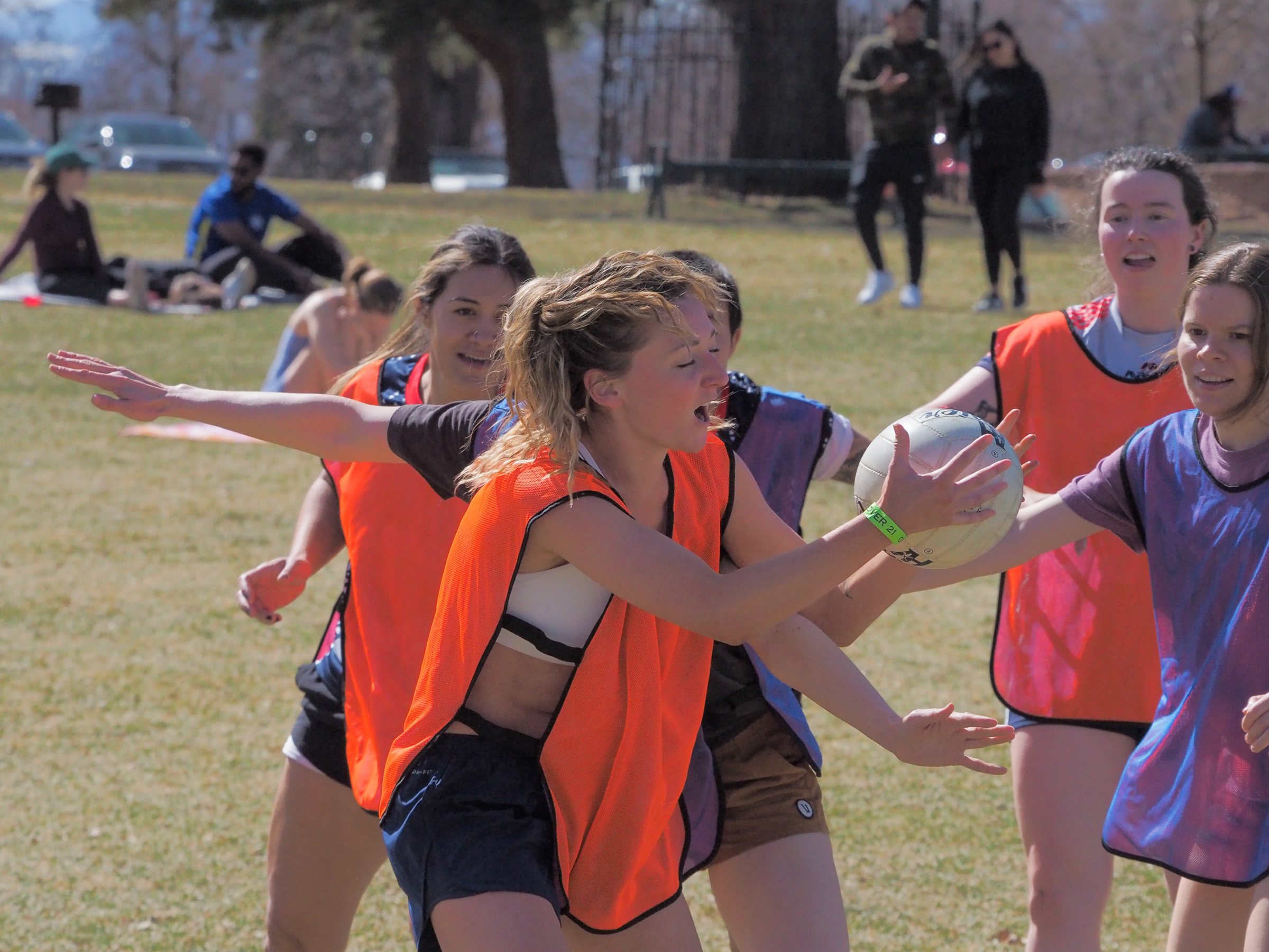 A woman wearing an orange hi-vis practice jersey catches a Gaelic football surrounded by other players.