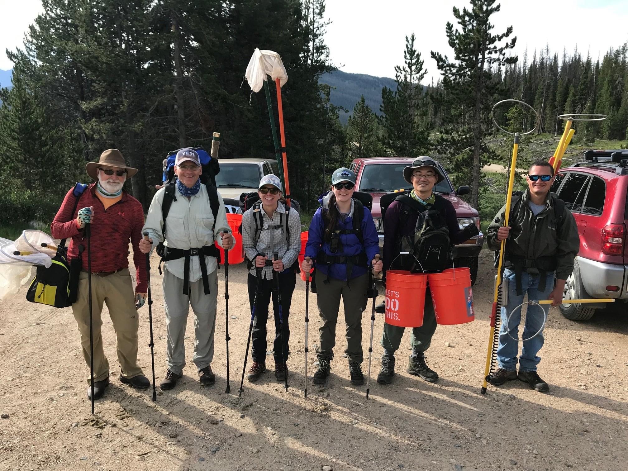 A group of people wearing backpacks and carrying nets and other tools pose for a photo.