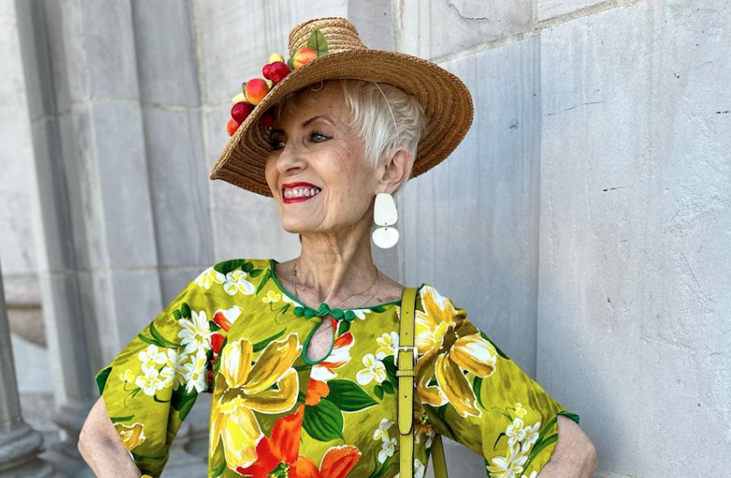 An older woman wears a large hat and a multi-color dress.